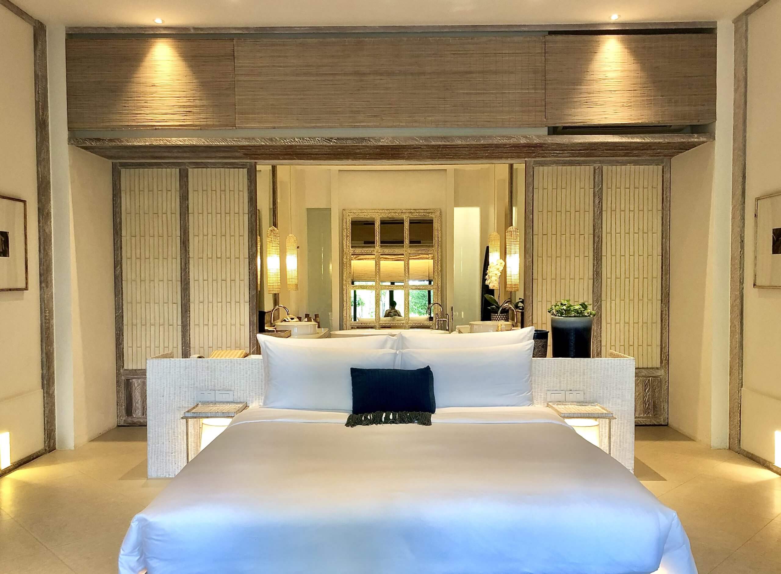 Ruime hotelkamer in warme crèmetinten, met een opgemaakt tweepersoonsbed, houten wandpanelen en zacht indirect licht